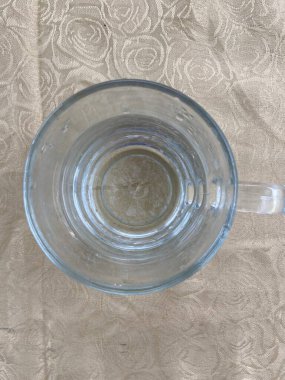 Su manzaralı cam. İçkiler masanın üstünde. Bej kırışık masa örtüsü.