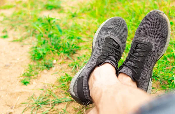 Kum ve yeşil çimlerden oluşan bir arka planda spor ayakkabısı giymiş bacaklar. çalışma sonrası dinlenme konsepti