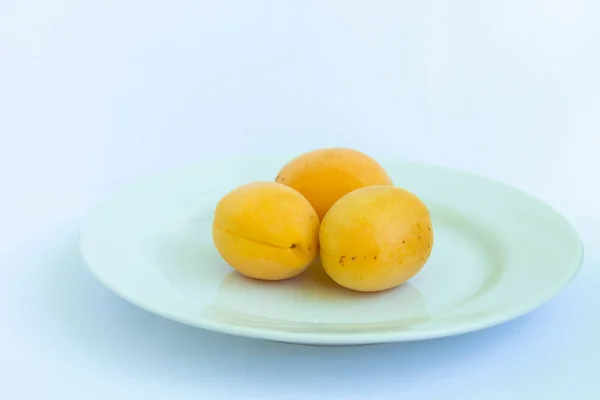 THREE FRUITS, persik, ON A WHITE CERAMIC PLATE DAN ON A WHITE BACKGROUND. konsep makanan sehat Stok Gambar Bebas Royalti