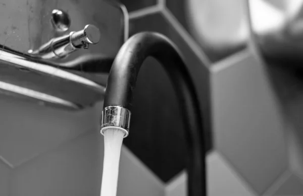 L'eau du robinet coule sur un fond de carrelage noir et blanc.. — Photo