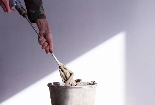 Stirrer di tangan seorang pekerja di semen mortir dan ember tua berkarat dekat Stok Foto Bebas Royalti