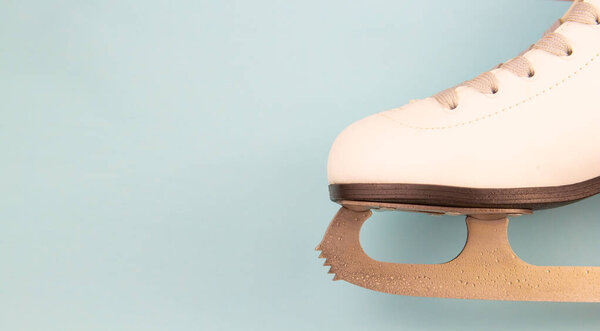 Белые коньки для фигурного катания лежат на синем фоне. Место для текста.