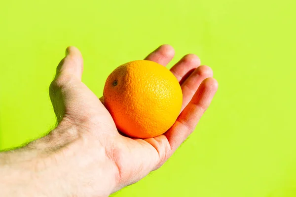 明るい光の中で男の手の近くの緑の背景にオレンジ — ストック写真