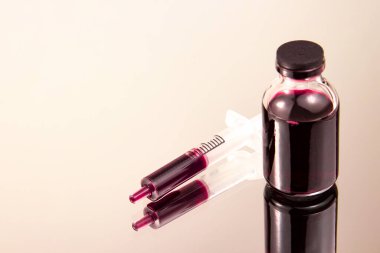 Tek kullanımlık şırınga ve kırmızı sıvı dolu bir kap. Kan testi.