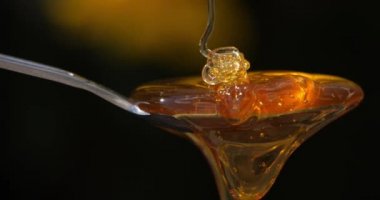 Siyah arka planda kaşığa dökülen bal