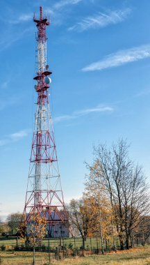 Telekomünikasyon kulesi antenli, mavi gökyüzünün arka planında, ağaçların yanındaki kırsal alanda