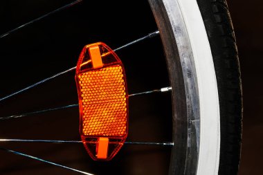 Büyük kırmızı plastik bir yansıtıcı. Bisiklet tekerleğinin üzerinde. Karanlıkta teller.