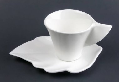 Siyah arka planda tabağı olan küçük beyaz bir fincan kahve.