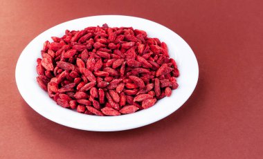 Kahverengi arka planda beyaz bir tabakta kurutulmuş goji üzümleri.