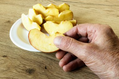 Ellerinde bir dilimle bir tabakta dilimlenmiş elma dilimleri.