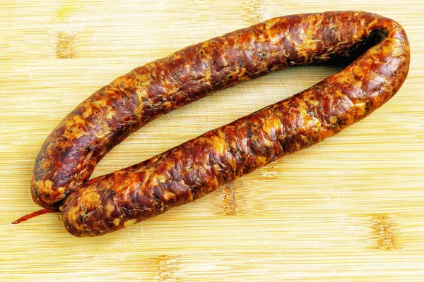 Cold smoked pork sausage ring on a bamboo cutting board