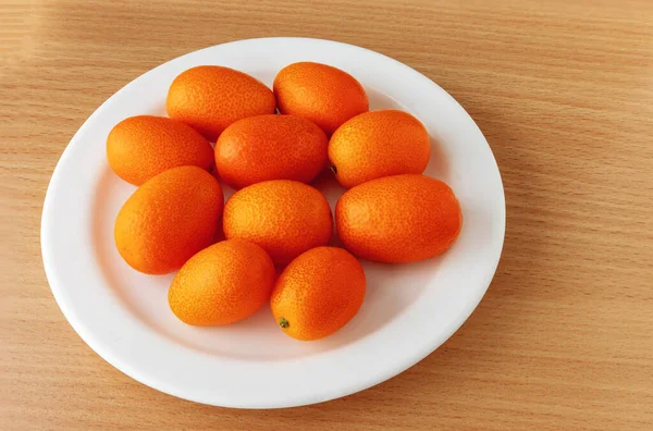 Fresh ripe kumquats in a white plate on the surface of an ash tree table