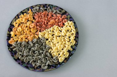 Gri arka planda koyu bir tabakta domates ve fesleğen aromalı dört renkli İtalyan makarnası.