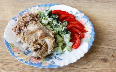 Haşlanmış domuz pirzolası, karabuğday, domates, dereotlu salatalık, ahşap bir masa yüzeyinde bir tabak.