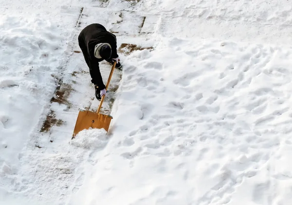 A guard in the yard of the house with a snow shovel removes snow