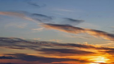 Güneş ufuktan batar, sıcak turuncu ve sarı renkler gökyüzünde yayılır. İnce bulutlar nazikçe süzülerek sakin akşam atmosferinin güzelliğini arttırır..