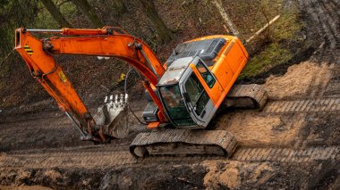 Bir inşaat alanında büyük sarı kazıcı, bir hendeğin yanında duruyor.