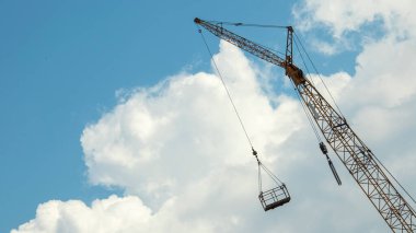 Mavi gökyüzüne karşı bir kule vinci, bir inşaat beşiği ile