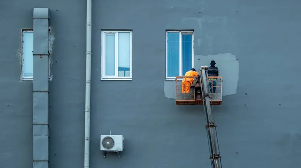 Dois pintores em um berço de construção pintam a fachada de um edifício Imagem De Stock