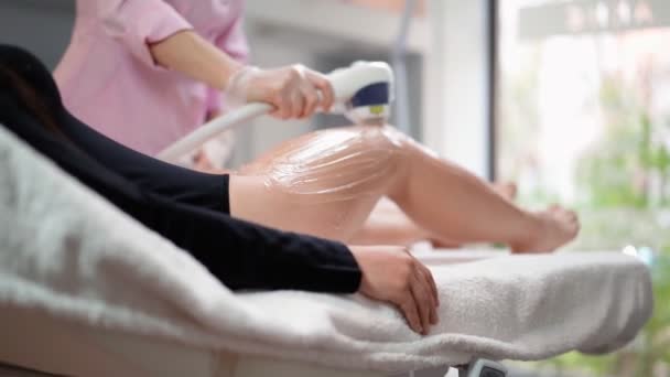 Kvinnlig kosmetolog gör laser hårborttagning på smala ben av vacker sexig kvinna som ligger på medicinsk soffa i skönhetssalong. Kosmitologi, epilering och spa koncept. Kroppsvård. Långsamma rörelser — Stockvideo