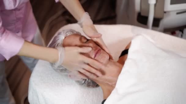 La esteticista femenina se prepara para el rejuvenecimiento por láser y la depilación facial de la mujer acostada en el sofá médico en el salón de belleza. Cosmitología, epiléptica y concepto de spa. Cuidado del cuerpo y la piel. Primer plano — Vídeo de stock