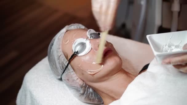 Kvinnlig kosmetolog förbereder sig för laserföryngring och ansiktshårborttagning av kvinna liggande på medicinsk soffa i skönhetssalong. Kosmitologi, epilering och spa koncept. Kropp och hudvård. Närbild — Stockvideo