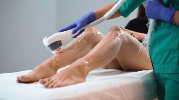 Kobieta kosmetyczka robi laserowe usuwanie włosów na szczupłych nogach pięknej młodej kobiety, która leży na medycznej kanapie w salonie piękności. Kosmitologia, depilacja i koncepcja spa. Opieka nad ciałem — Wideo stockowe