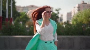 Uzun kızıl saçlı, gözlüklü ve turkuaz giysili güzel seksi bir kadın mutlulukla dans ediyor. Neşeli bayan başarıya sevinsin. Yavaş çekim.