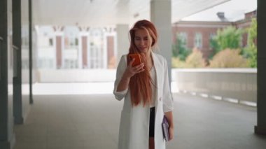 Güzel bir iş kadını gülümsüyor ve sokakta akıllı telefon mesajları kullanıyor. Şirketin yanındaki başarılı genç bayan telefonda mesaj yazıyor. Kadın girişimci e-postaları kontrol ediyor. Yavaş çekim.