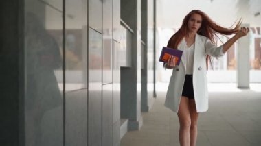 Moda elbiseli, kızıl saçlı, kendine güvenen güzel bir iş kadını işe yakın bir yerde yürüyor. Genç bayan başarılı bir şirket kariyeri yaşıyor. Zarif bayan girişimci şehir merkezinde yürüyor. Yavaş çekim.