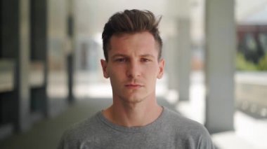 Bir şehir sokağının bulanık arka planında kameraya bakan yakışıklı bir adamın portresi. Çekici, beyaz bir adamın yüzüne yakın çekim. Yavaş çekim.