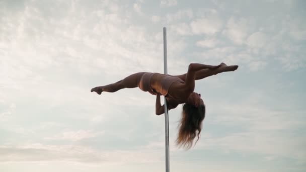 Mooie atletische vrouw voert trucs op de paal tegen de achtergrond van zonsondergang in het veld. Schoonheid en lichaamsverzorging. Vrouwelijke sport en fitness. Langzame beweging — Stockvideo