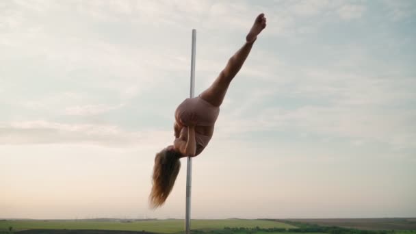 Mooie atletische vrouw voert trucs op de paal tegen de achtergrond van zonsondergang in het veld. Schoonheid en lichaamsverzorging. Vrouwelijke sport en fitness. Langzame beweging — Stockvideo