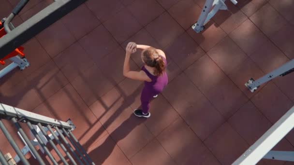 Mujer atlética joven en un chándal deportivo de color púrpura hace ejercicio se abalanza cruz en el terreno de entrenamiento en un parque de la ciudad. Fitness al aire libre. En cámara lenta. Vista superior — Vídeo de stock