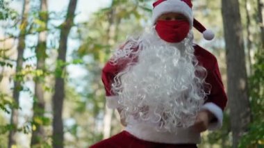 Noel Baba kostümü giymiş, yüzünde tıbbi maske olan oyuncu ormanda dans ediyor. Noel ve Coronavirus Covid-19 tatilleri boyunca karantina altındaydı. Yavaş çekim