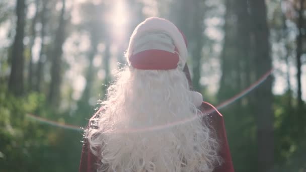身穿圣诞老人服装、头戴两个医疗面具的形象滑稽的男人站在森林中。圣诞节和验尸官。Covid-19 。假期期间的检疫。慢动作 — 图库视频影像