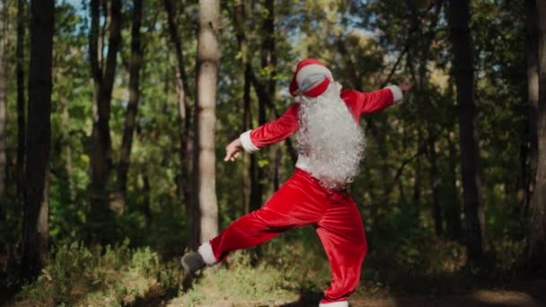 Brincalhão homem feliz vestido em terno Papai Noel com duas máscaras médicas em seu rosto engraçado dançando na floresta. Natal e coronavírus Covid-19 Quarentena durante as férias. Movimento lento — Vídeo de Stock