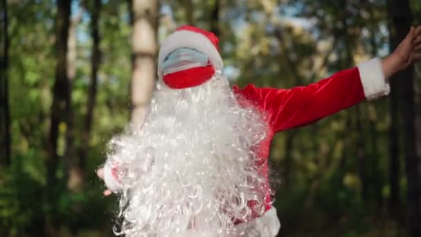 Brincalhão homem feliz vestido em terno Papai Noel com máscara médica em seu rosto engraçado dançando na floresta. Natal e coronavírus Covid-19 Quarentena durante as férias. Movimento lento — Vídeo de Stock