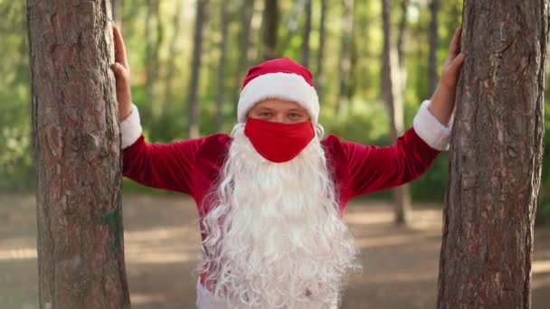 Um tipo vestido com um fato de Pai Natal com uma máscara médica protectora no rosto está sozinho na floresta. Coronavírus e Natal. Ano Novo durante a quarentena. Movimento lento — Vídeo de Stock