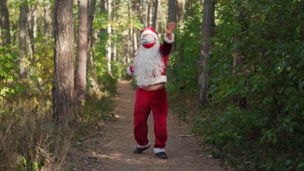 Juguetón hombre feliz vestido con traje de Santa Claus con dos máscaras médicas en su cara divertido baile en el bosque. Navidad y coronavirus Covid-19 Cuarentena durante las vacaciones. Movimiento lento — Vídeo de stock