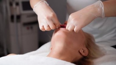 Kadın masör, genç ve güzel bayan müşteri sarışına yüz masajı ve ağız boşluğu yapar. Güzellik salonunda mükemmel cilt bakımı. Kozmetik servisi. Sağlık ve İlaç Hizmetleri