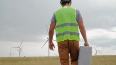 Üniformalı ve kasklı profesyonel ekoloji mühendisi elinde özel ekipmanlarla güzel bir arka planda yel değirmenine hizmet ediyor. Alternatif enerji ve Rüzgar santrali.