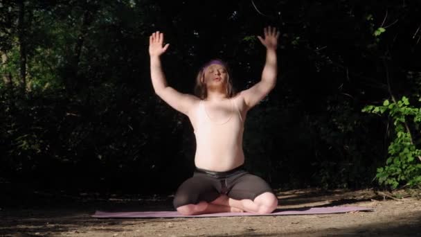 穿着紧身衣 留着长发的快乐的胖子在健身垫上做瑜伽 在森林里进行户外训练的怪物 — 图库视频影像