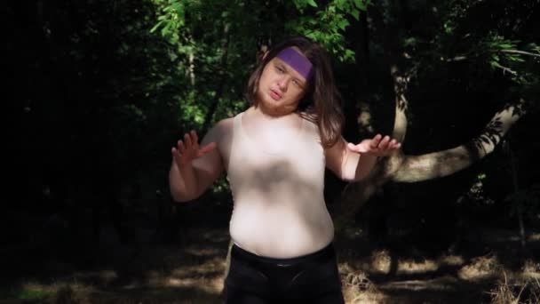 穿着紧身T恤 留着一头长发的爱玩耍的胖子在户外体重减轻体重 有趣的超重的家伙描述了一个在森林里锻炼的女孩 运动幽默概念 慢动作 — 图库视频影像
