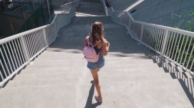 Mutlu Neşeli Kadın merdivenlerden sırt çantasıyla iniyor. O, kısa şort ve bir üst giyiyor. İş merkezinin yanındaki Şehir Parkı 'nda çekilmiş. Ağır çekim. Havadan ateş ediyorlar...