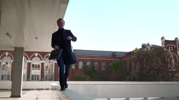 Happy crazy business man walks and dances funny on parapet in downtown. Entrepreneur with folder documents in his hand jumping for joy. Office worker and successful corporate career. Slow motion — Stock Video