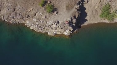 Hava görüntüsü. Kaslı adam uçurumdan kristal berrak deniz suyuna atlar ve yüzer.