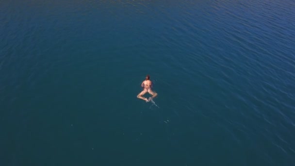 Vista aérea. hermosa mujer con figura delgada en traje de baño nada en mar de cristal — Vídeo de stock