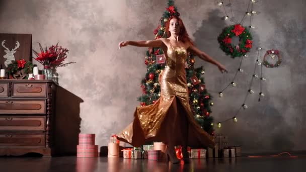 Όμορφη γυναίκα σε χρυσό βραδινό φόρεμα περιστρέφεται και χορεύει κοντά στο χριστουγεννιάτικο δέντρο — Αρχείο Βίντεο