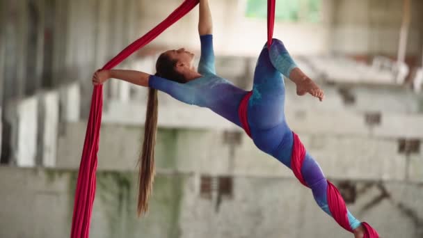 Atlética mujer elegante aerialista con un tramo pronunciado en overoles deportivos hace un truco acrobático en lienzos rosados en el edificio abandonado de fondo. Deporte extremo. Estilo de vida saludable. Movimiento lento — Vídeos de Stock